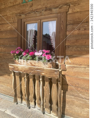 Traditional alpine wooden house wall facade with a window and a flower box filled with blooming pink geraniums in Hausham, Upper Bavaria, Germany. Traditional alpine wooden house wall facade with a window and a flower box filled with blooming pink geraniums in Hausham, Upper Bavaria, Germany. 142340300