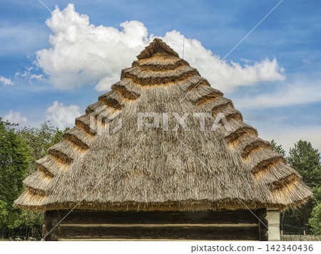 Traditional Thatched Roof Cottage With Layered Straw Thatch Against Blue Sky Traditional Thatched Roof Cottage With Layered Straw Thatch Against Blue Sky 142340436