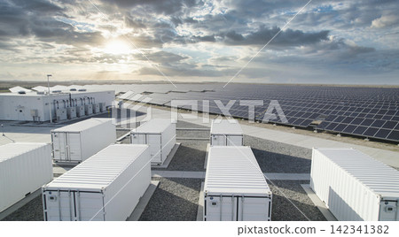 Modern solar farm with battery storage containers and vast solar panel array under cloudy sky Modern solar farm with battery storage containers and vast solar panel array under cloudy sky 142341382