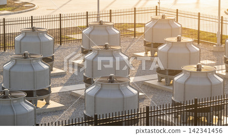 Industrial cooling towers lined up on a gravel surface under warm sunlight Industrial cooling towers lined up on a gravel surface under warm sunlight 142341456