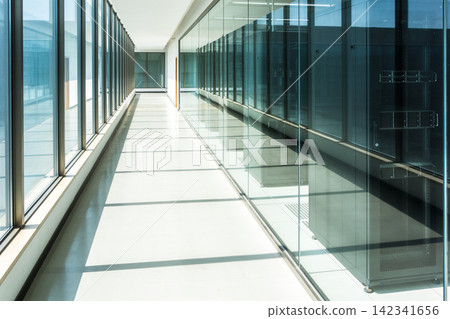 Modern glass corridor with server racks and natural light creating geometric shadows Modern glass corridor with server racks and natural light creating geometric shadows 142341656