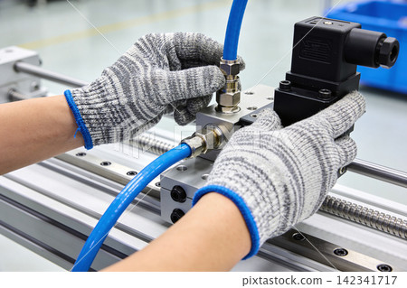 Hands in protective gloves assembling pneumatic system components in a factory setting Hands in protective gloves assembling pneumatic system components in a factory setting 142341717