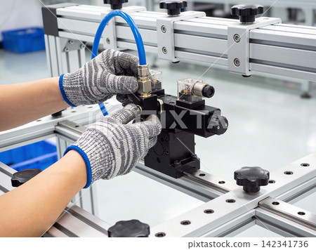 Hands in protective gloves assembling a pneumatic valve system on an industrial frame Hands in protective gloves assembling a pneumatic valve system on an industrial frame 142341736