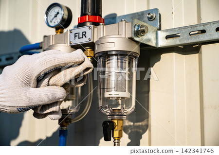 Maintenance worker cleaning an industrial air filter regulator unit with a cloth Maintenance worker cleaning an industrial air filter regulator unit with a cloth 142341746