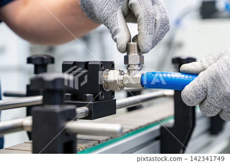 Worker in protective gloves assembling industrial plumbing fittings on a conveyor belt Worker in protective gloves assembling industrial plumbing fittings on a conveyor belt 142341749