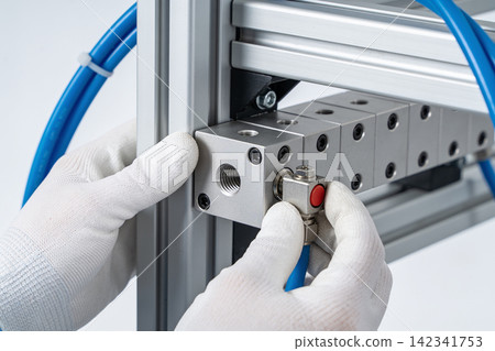 Technician installs pneumatic manifold block with blue tubing on aluminum extrusion frame Technician installs pneumatic manifold block with blue tubing on aluminum extrusion frame 142341753