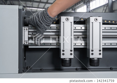 Close-up of a gloved hand adjusting precision linear motion components on industrial machinery Close-up of a gloved hand adjusting precision linear motion components on industrial machinery 142341759