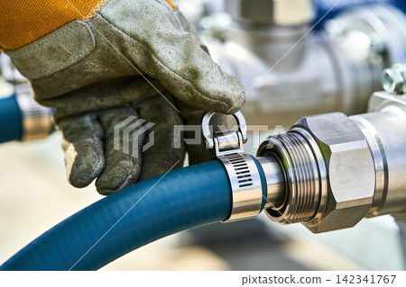 Worker in protective glove secures hose connection with metal clamp on industrial equipment Worker in protective glove secures hose connection with metal clamp on industrial equipment 142341767