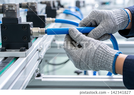 Technician wearing gloves connects blue pneumatic tube to industrial machinery Technician wearing gloves connects blue pneumatic tube to industrial machinery 142341827