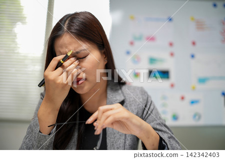 Businesswoman experiencing eye strain and work fatigue rubbing eyes and removing glasses for stress relief in office workplace Businesswoman experiencing eye strain and work fatigue rubbing eyes and removing glasses for stress relief in office workplace 142342403