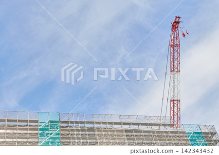 The exterior of a high-rise building under construction and a large crane reaching towards the blue sky. The exterior of a high-rise building under construction and a large crane reaching towards the blue sky. 142343432