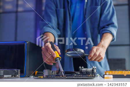 Computer technician using magnifying glass to inspect computer mainboard for repairing or upgrading. Computer technician using magnifying glass to inspect computer mainboard for repairing or upgrading. 142343557
