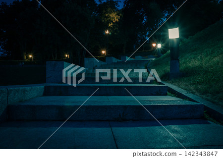 The tiled stairs in the night green park with lanterns in summer. Benches in the park during the summer season at night. Illumination of a park road with lanterns. Park of Eternal Glory. Ukraine The tiled stairs in the night green park with lanterns in summer. Benches in the park during the summer season at night. Illumination of a park road with lanterns. Park of Eternal Glory. Ukraine 142343847