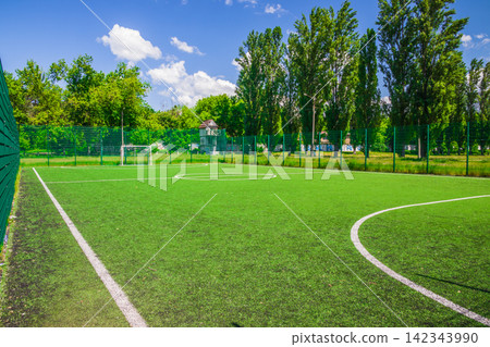 Soccer field with artificial green grass near the school. Amateur football field. Sunny summer day Soccer field with artificial green grass near the school. Amateur football field. Sunny summer day 142343990