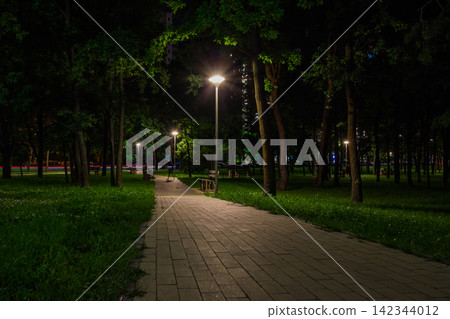 The tiled road in the night green park with lanterns in spring. A benches in the park during the spring season at night. Illumination of a park road with lanterns at night. Mariinsky Park. Ukraine The tiled road in the night green park with lanterns in spring. A benches in the park during the spring season at night. Illumination of a park road with lanterns at night. Mariinsky Park. Ukraine 142344012