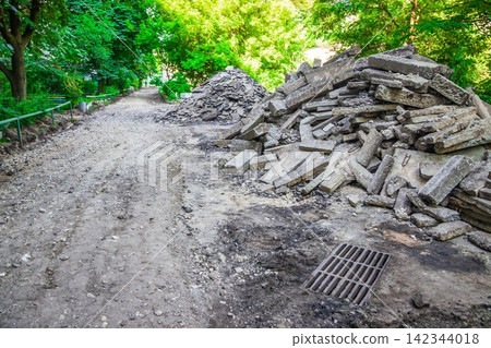 A pile of broken asphalt near the road under reconstruction. Reconstruction of the road near the old high house A pile of broken asphalt near the road under reconstruction. Reconstruction of the road near the old high house 142344018