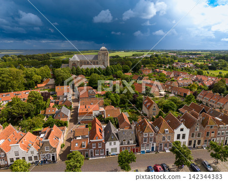 High angle wide horizontal aerial drone photograph of Grote Kerk church, historic orange roofs, town landscape, and dramatic storm sky in Veere, Zeeland, Netherlands on sunny summer day High angle wide horizontal aerial drone photograph of Grote Kerk church, historic orange roofs, town landscape, and dramatic storm sky in Veere, Zeeland, Netherlands on sunny summer day 142344383
