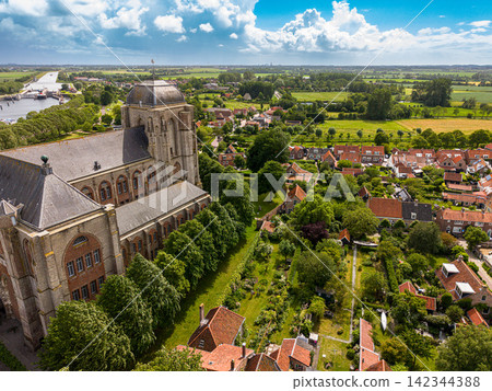 High angle wide horizontal aerial drone photograph of Grote Kerk church, lush green gardens, historic houses, canal locks, polder landscape, and cloudy sky in Veere, Zeeland, Netherlands on sunny day High angle wide horizontal aerial drone photograph of Grote Kerk church, lush green gardens, historic houses, canal locks, polder landscape, and cloudy sky in Veere, Zeeland, Netherlands on sunny day 142344388