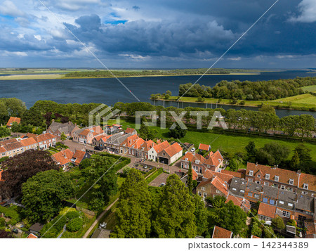 High angle wide horizontal aerial drone photograph of historic orange roofs, Lake Veere shoreline, green polder landscape, and dramatic storm sky in Veere, Zeeland, Netherlands on sunny summer day High angle wide horizontal aerial drone photograph of historic orange roofs, Lake Veere shoreline, green polder landscape, and dramatic storm sky in Veere, Zeeland, Netherlands on sunny summer day 142344389