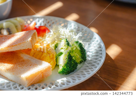 一張沐浴在暖光下的西式早餐盤和一張木桌的特寫。 142344773