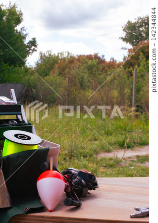 Fishing equipment on a wooden surface with a bobber, reel, and spool of line, preparing for an outdoor angling hobby in a natural setting Fishing equipment on a wooden surface with a bobber, reel, and spool of line, preparing for an outdoor angling hobby in a natural setting 142344844