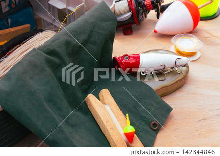 Fishing gear arranged on a wooden surface, showing lures, fishing line, bobbers, and a reel, representing an outdoor hobby and recreational activity Fishing gear arranged on a wooden surface, showing lures, fishing line, bobbers, and a reel, representing an outdoor hobby and recreational activity 142344846