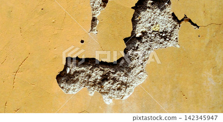 Cracked yellow stucco wall with a damaged plaster texture. Cracked yellow stucco wall with a damaged plaster texture. 142345947