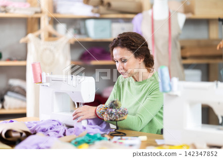 Female tailor using sewing machine to make garment in studio Female tailor using sewing machine to make garment in studio 142347852
