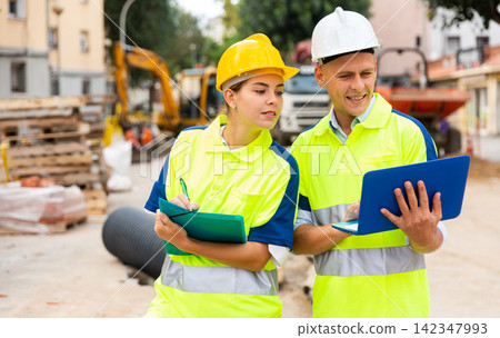 Two engineers are discussing an important project, holding a laptop and an estimate Two engineers are discussing an important project, holding a laptop and an estimate 142347993