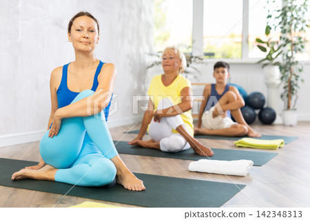 Middle-aged woman practicing lord of the fishes pose of yoga in light fitness room 142348313