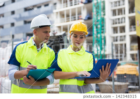 Two engineers are discussing an important project, holding a laptop and an estimate Two engineers are discussing an important project, holding a laptop and an estimate 142348315