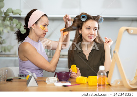 Adult woman curls hair of young woman Adult woman curls hair of young woman 142348325