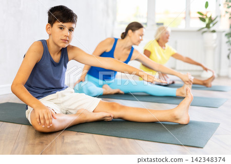 Preteen boy practicing head to knee pose of yoga in light fitness room Preteen boy practicing head to knee pose of yoga in light fitness room 142348374