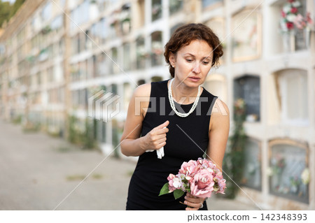 Sorrowful woman puts bouquet of hydrangeas on grave of deceased friend, mourns loss Sorrowful woman puts bouquet of hydrangeas on grave of deceased friend, mourns loss 142348393