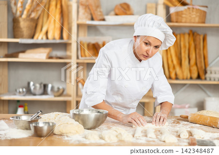 Female baker preparing croissant dough - kneading, rolling and cutting dough on table in bakery Female baker preparing croissant dough - kneading, rolling and cutting dough on table in bakery 142348487