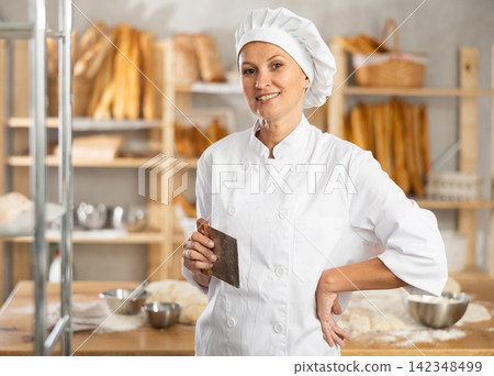 Woman baker cook stands against background of workspace with cutter Woman baker cook stands against background of workspace with cutter 142348499