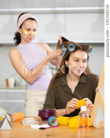 Adult woman curls hair of young woman Adult woman curls hair of young woman 142348516