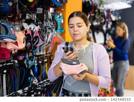Young woman scanning label on dog outfits in pet store 142348533