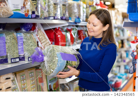 Young woman choosing straw bedding for rabbits at pet store Young woman choosing straw bedding for rabbits at pet store 142348565