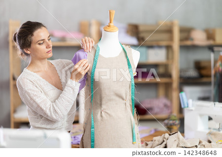 Woman tailor connects parts of dress on mannequin Woman tailor connects parts of dress on mannequin 142348648