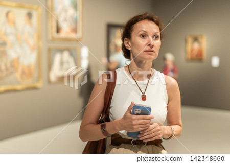 Positive woman visitor with smartphone in hands exploring religious art in museum Positive woman visitor with smartphone in hands exploring religious art in museum 142348660