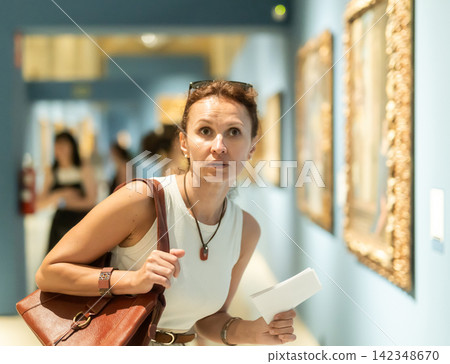 Woman viewing art gallery with brochure Woman viewing art gallery with brochure 142348670