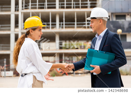 Man and woman in hardhats shaking hands in construction site 142348698