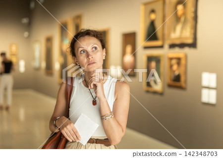 Interested woman in casual clothes exploring paintings in halls of museum Interested woman in casual clothes exploring paintings in halls of museum 142348703