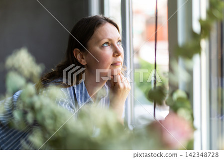 Portrait of dreaming woman at the window in house Portrait of dreaming woman at the window in house 142348728