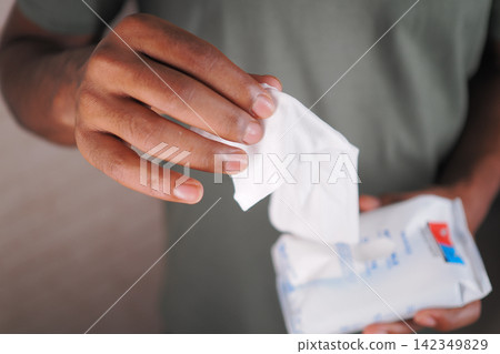 A person takes out a wet tissue from a packet in a room at home A person takes out a wet tissue from a packet in a room at home 142349829