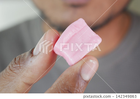 Man holds a piece of pink gum close to his face Man holds a piece of pink gum close to his face 142349863
