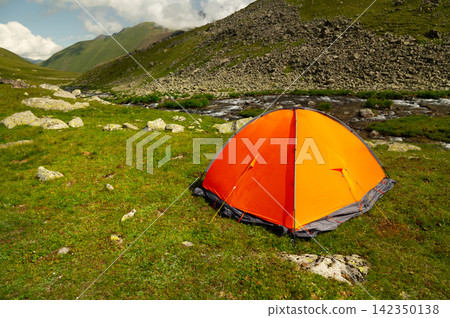 Bright orange camping tent pitched on green grassy meadow Bright orange camping tent pitched on green grassy meadow 142350138