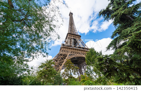 Low angle view of eiffel tower framed by green trees under blue sky in paris france Low angle view of eiffel tower framed by green trees under blue sky in paris france 142350415