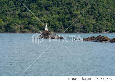 Ban Hua Laem Chedi, a white Buddhist stupa standing on rocky outcrop in the sea at Chanthaburi, Thailand, surrounded by tropical forest as a sacred coastal landmark. Local faith, culture and heritage. Ban Hua Laem Chedi, a white Buddhist stupa standing on rocky outcrop in the sea at Chanthaburi, Thailand, surrounded by tropical forest as a sacred coastal landmark. Local faith, culture and heritage. 142350529